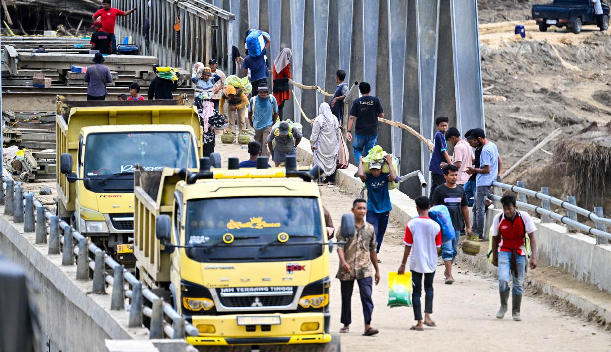 Diketahui, hingga kini, pemerintah melalui Kementerian Pekerjaan Umum dan Perumahan Rakyat (PUPR) bersama TNI/Polri serta warga setempat terus bergerak cepat membangun jembatan bailey sebagai solusi darurat. Tampak dalam foto, warga menyeberangi sungai di jembatan yang baru dibangun yang menghubungkan Aceh dan Provinsi Sumatera Utara setelah hancur akibat banjir bandang di Sungai Peusangan, Distrik Bireuen, Provinsi Aceh, Selasa 9 Desember 2025. (CHAIDEER MAHYUDDIN/AFP)
