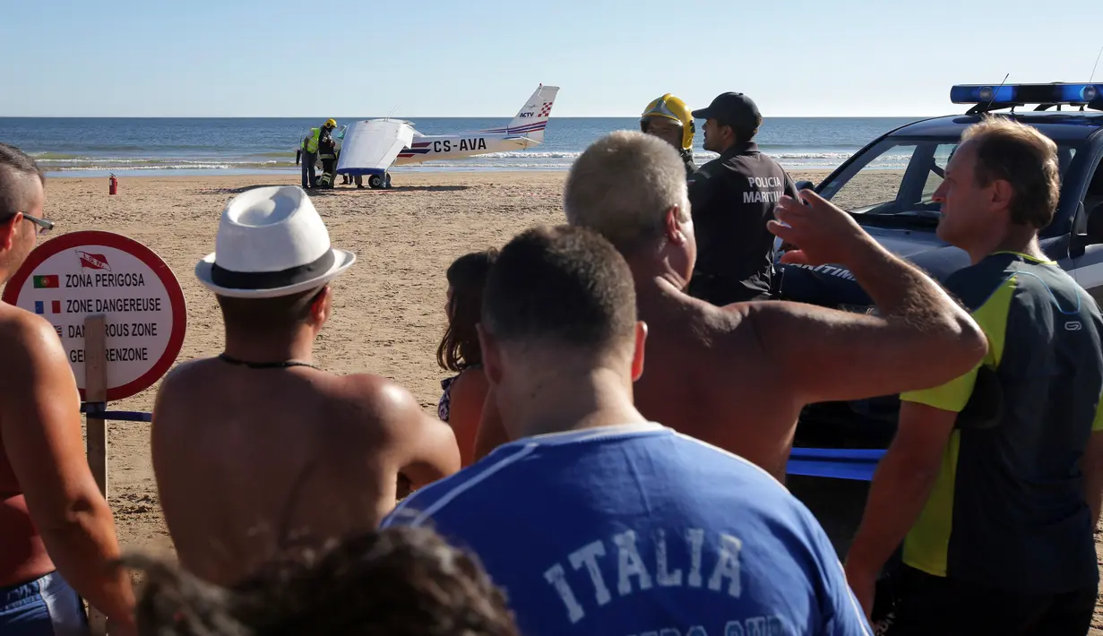 Sejumlah orang berkumpul melihat sebuah pesawat kecil yang mendarat darurat di pantai Sao Joao yang ramai dekat Lisbon, Portugal, Rabu (2/8). Kedua penumpang pesawat dilaporkan tidak terluka dan diinterogasi oleh pihak berwenang. (AP Photo/Armando Franca)