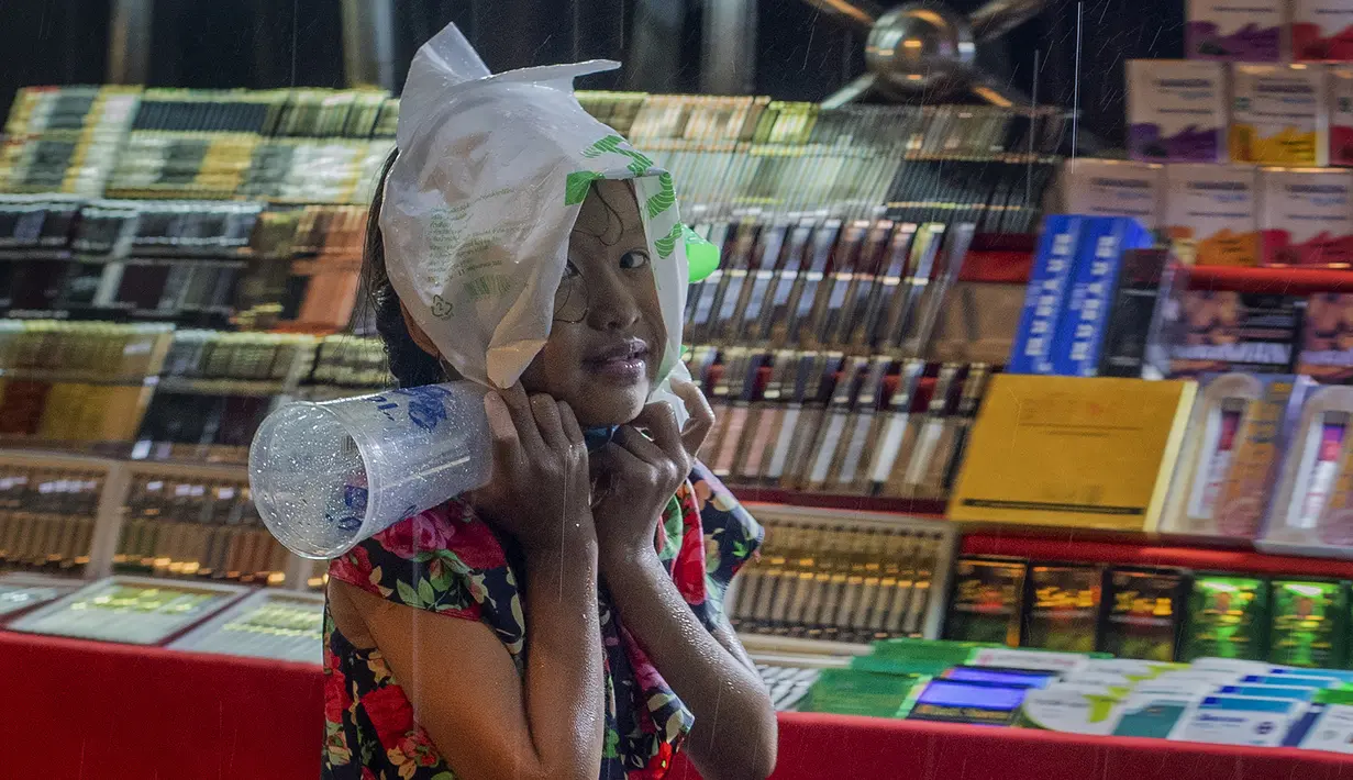 Seorang anak menerjang hujan dengan kantong plastik saat dia mencoba mengumpulkan uang di Bangkok, Thailand, Rabu (17/6/2020). Keseharian warga Bangkok berangsur normal setelah pemerintah terus melonggarkan pembatasan terkait pandemi virus corona COVID-19. (AP Photo/Gemunu Amarasinghe)