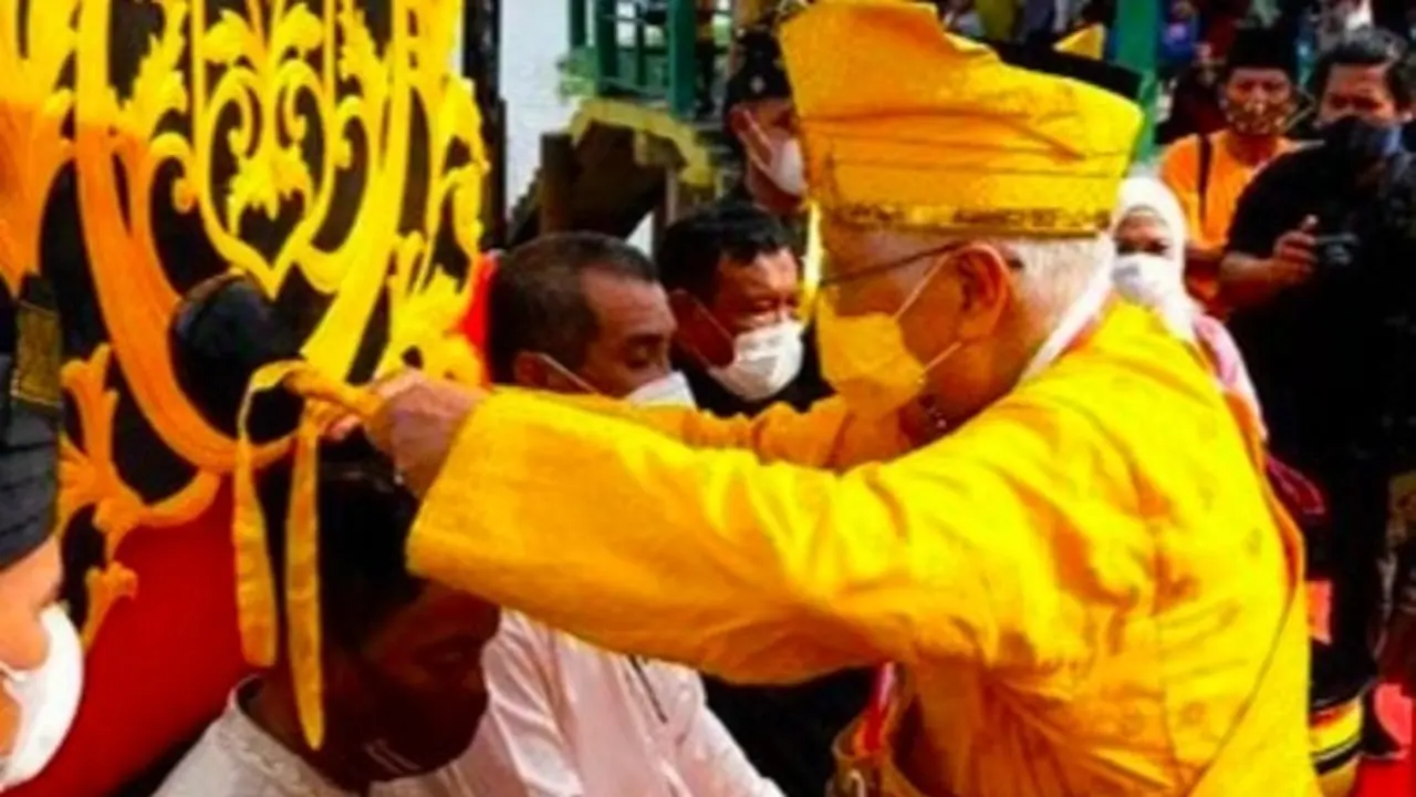 Sultan Kerajaan Pelalawan menyiram kepala tokoh adat dengan air bercampur bunga dan akar.