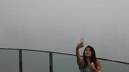 Seorang wanita berselfie dengan latar belakang pemandangan distrik pusat bisnis Singapura yang diselimuti kabut asap, Senin (14/9/2015). Singapura tak luput terkena dampak kabut asap pembakaran lahan di Pulau Sumatera. (REUTERS/Edgar Su)