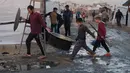 Situasi ini menghambat upaya pemulihan. Tampak dalam foto, pengungsi Palestina berjalan melalui jalan-jalan berlumpur sementara seorang pria dan anak-anak membawa peralatan masak di sebuah kamp di Jabalia, di bagian utara Jalur Gaza, Minggu 7 Desember 2025. (AP Photo/Jehad Alshrafi)
