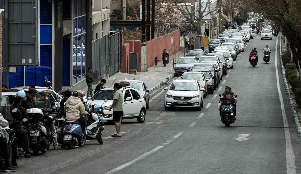 Serangan udara dan rudal menargetkan lima kota besar di Iran, termasuk ibu kota Teheran, serta lokasi strategis di Isfahan, Tabriz, Karaj, dan wilayah lainnya. Tampak dalam foto, orang-orang mengantre untuk mengisi bahan bakar mobil dan sepeda motor mereka di luar sebuah SPBU di Teheran, Iran pada Sabtu 28 Februari 2026. (Atta KENARE/AFP)
