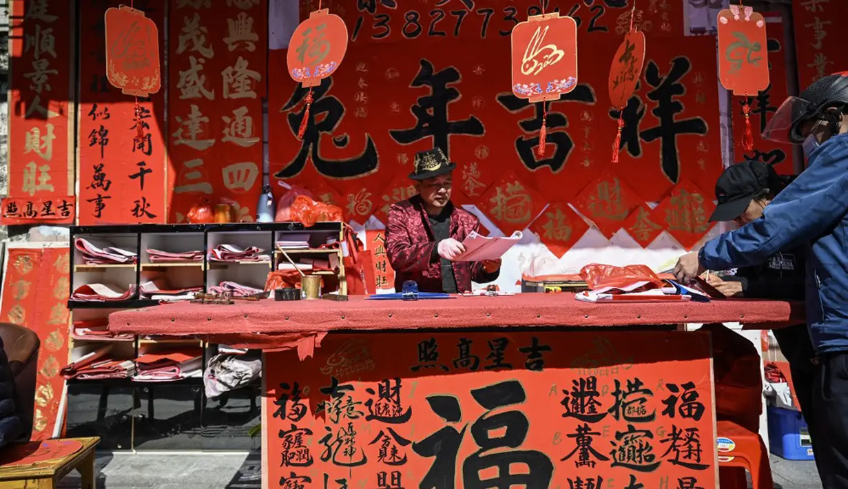 Seorang kaligrafer menulis kuplet musim semi, semacam dekorasi Tahun Baru Imlek, jelang dimulainya Tahun Baru Imlek di sebuah kios di Foshan, Provinsi Guangdong, China, 18 Januari. Dua baris kuplet yang biasanya terdiri dari tujuh atau sembilan karakter ditempelkan pada kedua sisi ambang pintu. (Giok Gao/AFP)
