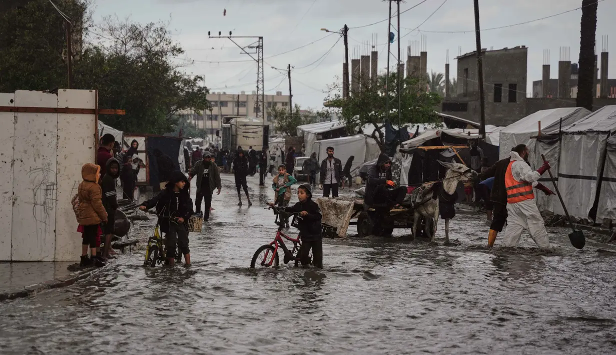 Warga Palestina berjalan di jalanan yang terendam banjir di samping kamp tenda sementara setelah hujan deras di Deir al-Balah, Jalur Gaza tengah, Selasa 25 November 2025. Banjir kembali menggenangi sebagian wilayah Deir al-Balah, Jalur Gaza tengah, pada Selasa 25 November 2025. (AP Photo/Abdel Kareem Hana)