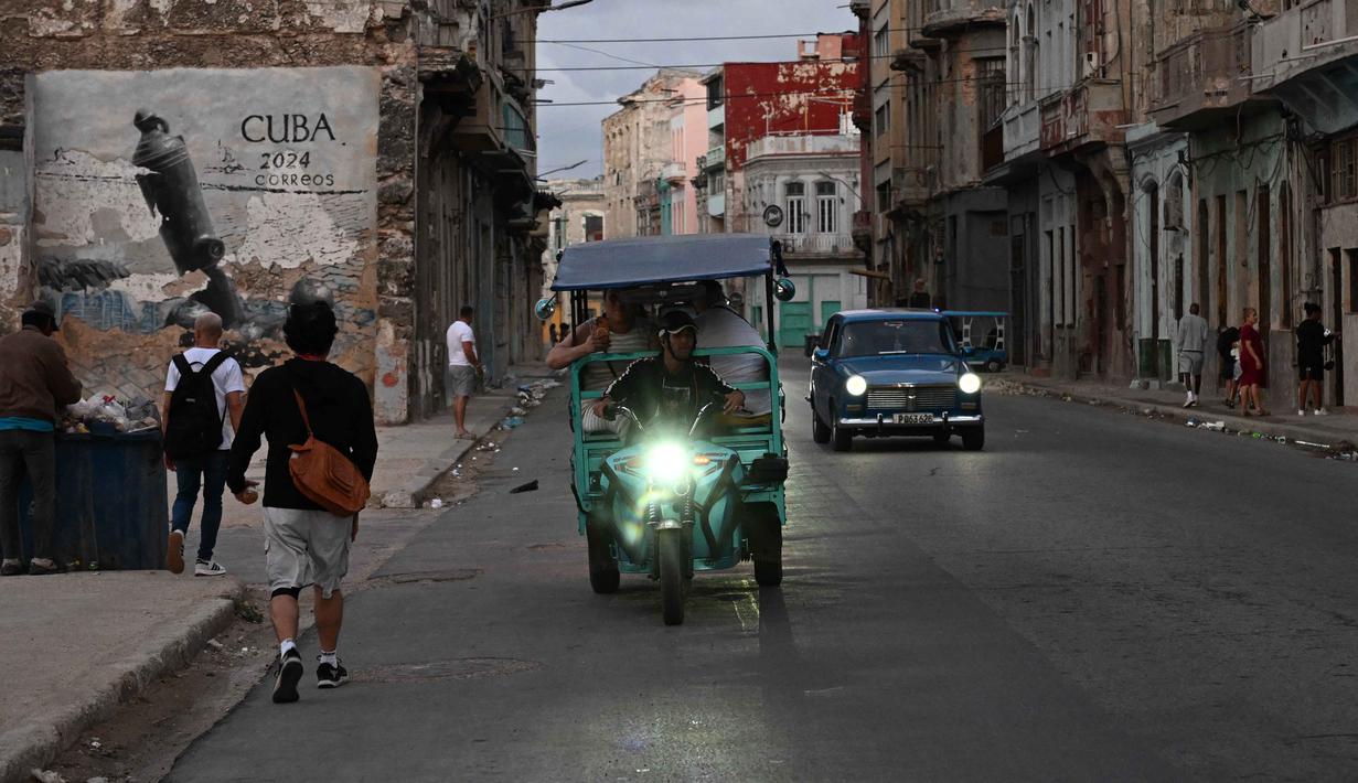 Kejadian ini memperparah krisis energi di Kuba yang disebabkan oleh infrastruktur yang sudah tua dan kekurangan bahan bakar akibat blokade minyak yang diperketat oleh Amerika Serikat. Tampak dalam foto, orang-orang beraktivitas di jalanan tanpa aliran listrik selama pemadaman listrik nasional di Havana, Kuba pada Sabtu 21 Maret 2026. (Yamil LAGE/AFP)