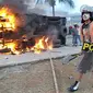 Seorang warga menggunakan perlengkapan Satpol PP berjalan melintasi truk yang terbakar usai terjadinya bentrokan antara Satpol PP dengan warga di sekitar Koja, Tanjung Priok(Antara)