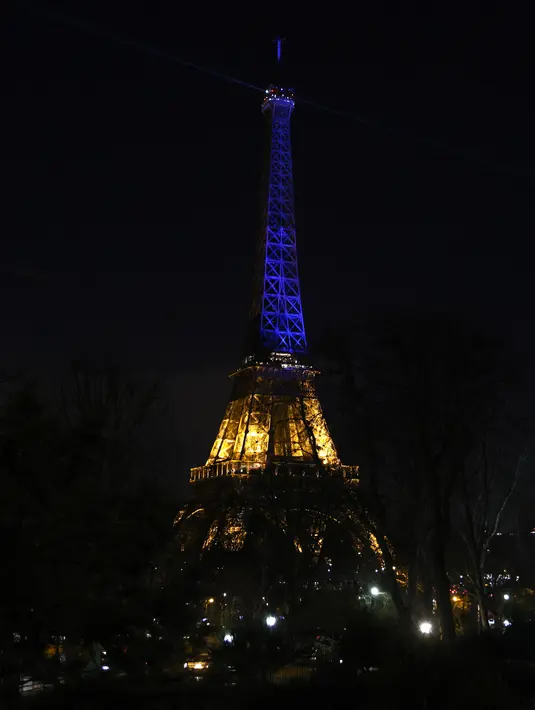 Menara Eiffel menyala dengan warna biru dan kuning, warna bendera Ukraina di Paris (25/2/2022). Pasukan Rusia menyerang ibu kota Ukraina pada Jumat (25/2) dengan tembakan dan ledakan dalam invasi ke negara demokratis yang memicu kekhawatiran perang yang lebih luas di Eropa. (AFP/ Thomas Coex)