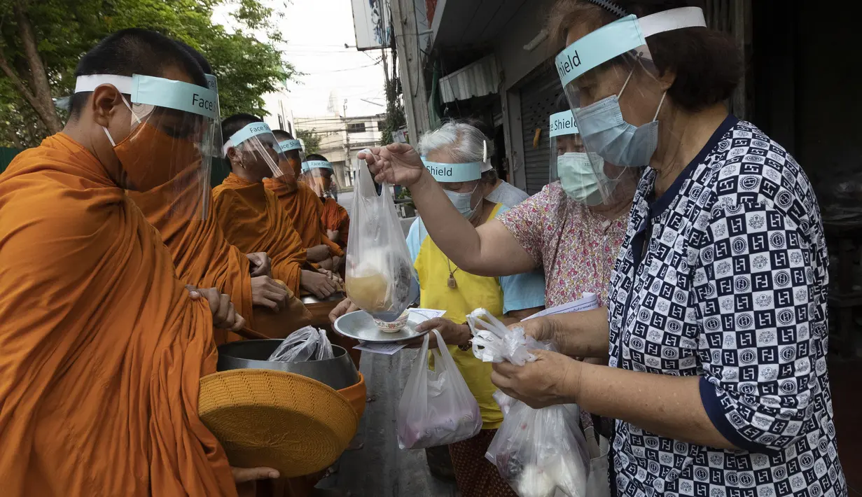 Warga menyerahkan makanan kepada para biksu Buddha yang memakai pelindung wajah untuk melindungi diri dari virus corona COVID-19 saat mengumpulkan sedekah di Bangkok, Thailand, Selasa (31/3/2020). Hingga 30 Maret 2020, jumlah kasus positif COVID-19 di Thailand ada 1.524. (AP Photo/Sakchai Lalit)
