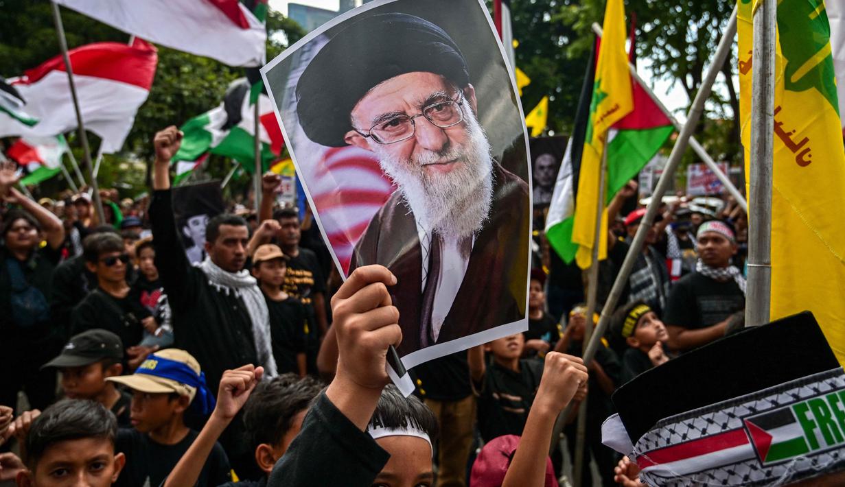 Seorang anak laki-laki memegang plakat bergambar pemimpin tertinggi Iran, Ayatollah Ali Khamenei yang gugur dalam serangan Amerika Serikat dan Israel pada akhir Februari lalu, selama berunjuk rasa memperingati Hari Al-Quds, di Surabaya, Jawa Timur, Jumat (13/3/2026). Ratusan orang turun ke jalan menggelar aksi unjuk rasa memperingati Hari Al-Quds Internasional. (Juni KRISWANTO/AFP)