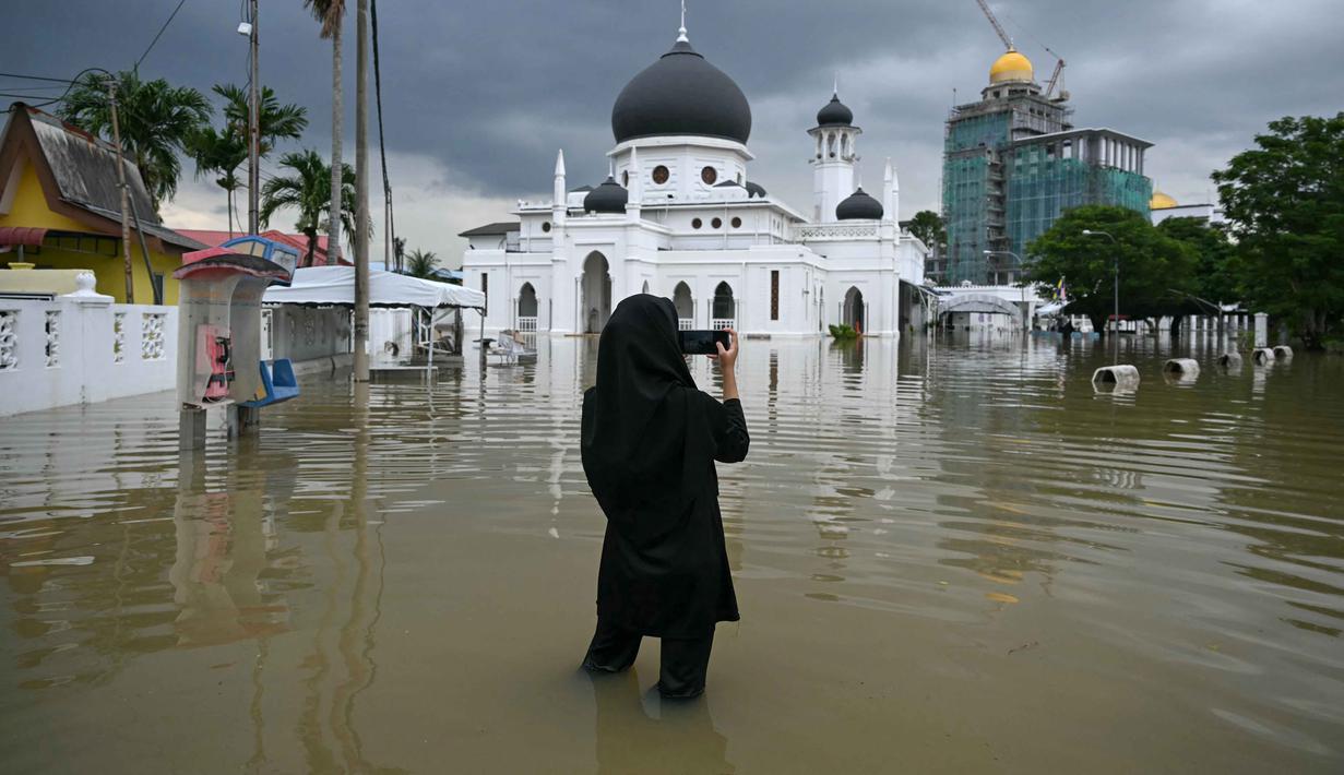 Faktor-faktor lain terkait lahan seperti perubahan penggunaan lahan, kepadatan populasi, dan efektivitas sistem drainase lokal ikut memengaruhi terjadinya bencana banjir di Malaysia. Tampak dalam foto, seorang perempuan mengambil dokumentasi masjid yang terendam banjir di Kangar, negara bagian Perlis, Malaysia utara, pada Kamis 27 November 2025. (Mohd RASFAN/AFP)