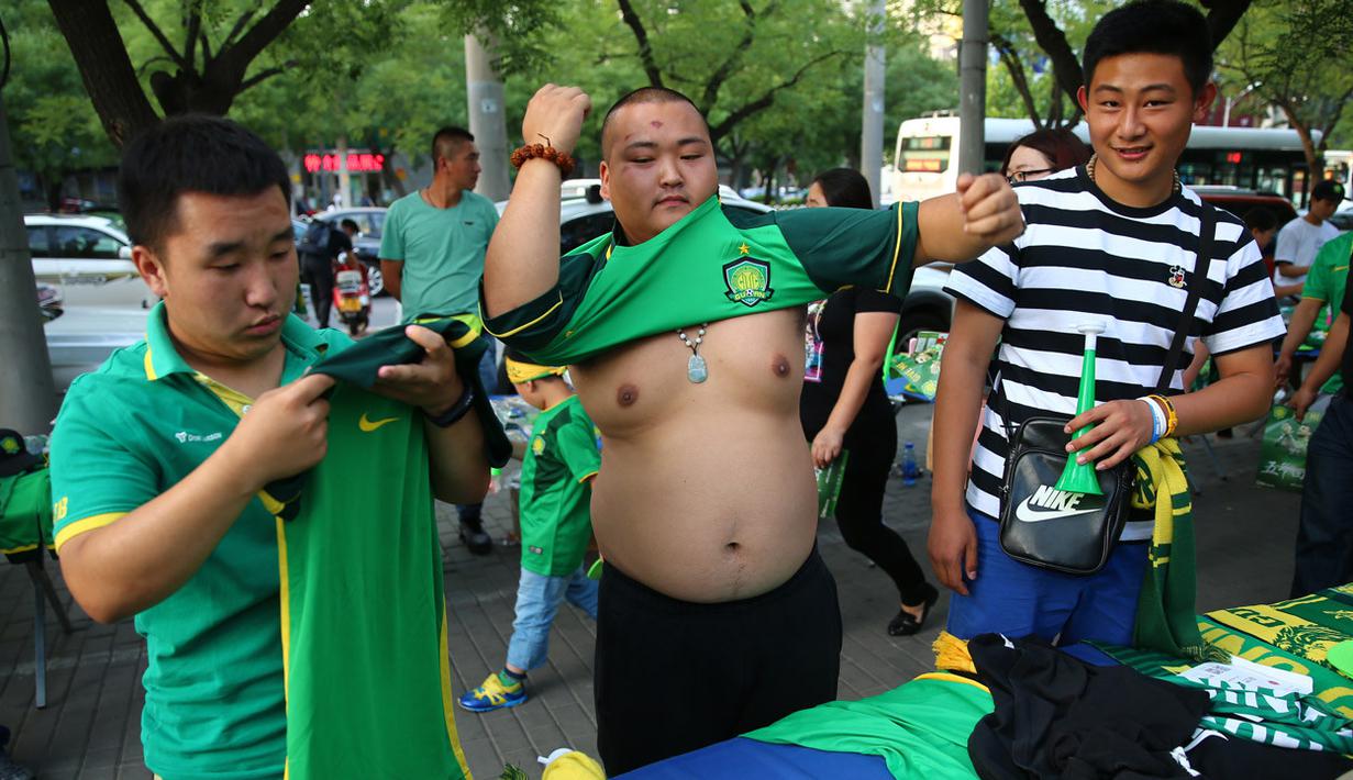 Suporter klub Beijing Guoan FC mencoba atribut klub yang dijual pedagang kaki lima di sekitar area stadion.(EPA/Wu Hong)