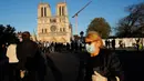 Seorang perempuan melintasi orang-orang yang berhenti di depan Katedral Notre Dame saat kembali membunyikan lonceng utamanya di Paris, Rabu (15/4/2020). Lonceng utama katedral kembali dibunyikan setelah satu tahun mengalami kebakaran yang sampai mengejutkan seluruh warga dunia. (AP/Christophe Ena)
