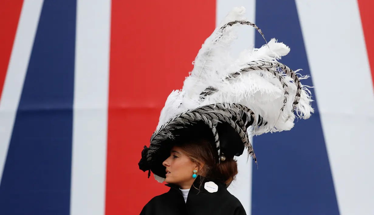 Seorang wanita mengenakan topi atau fascinator unik bermotif bulu melintas di depan bendera Union Jack saat menghadiri ajang pacuan kuda Royal Ascot di Ascot, Inggris, Selasa (18/6/2019). Royal Ascot menjadi ajang bagi wanita Inggris untuk tampil dengan fascinator unik. (AP Photo/Alastair Grant)