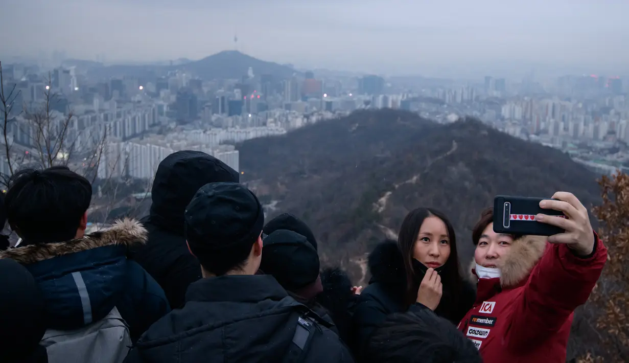 Pasangan berselfie di sudut pandang yang menghadap ke cakrawala kota untuk menyaksikan matahari terbit pertama tahun baru, meskipun dalam kondisi mendung, di Seoul, Korea Selatan (1/1/2020). (AFP/Ed Jones)