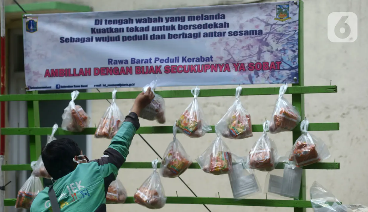 Pengemudi ojek online mengambil sembako yang digantung di rak kayu di kawasan Rawa Barat, Jakarta Selatan, Kamis (14/5/2020). Selama masa pandemi COVID-19, pihak kelurahan dan masjid sekitar menyediakan paket berisi mi instan, telur, dan masker untuk warga yang membutuhan. (merdeka.com/Imam Buhori)