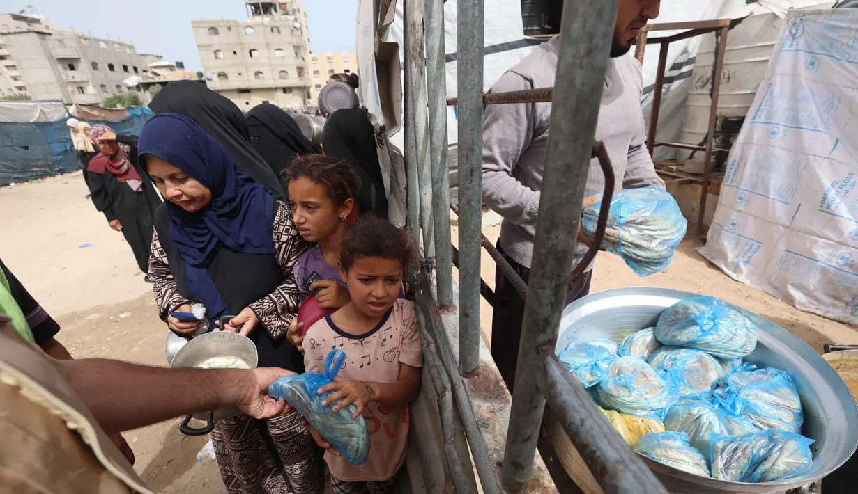 Seorang anak pengungsi Palestina mengambil sebungkus roti sementara yang lain menunggu giliran mereka dari salah satu dapur amal di kamp pengungsi Bureij, Jalur Gaza Tengah pada Senin 18 Mei 2026. (Eyad Baba/AFP)