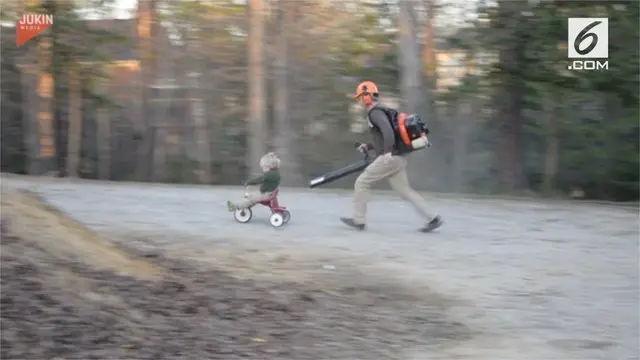 Seorang ayah yang membantu anaknya bermain sepeda roda tiga dengan blower daun.