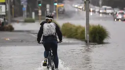 Seorang pengendara sepeda melewati banjir di Auckland, Selandia Baru, Rabu (1/2/2023). Peringatan hujan lebat untuk Auckland dicabut, meskipun keadaan darurat tetap berlaku untuk kota terbesar di negara itu setelah rekor curah hujan dan banjir pada hari Jumat menewaskan empat orang orang dan menyebabkan gangguan yang meluas. (Dean Purcell/New Zealand Herald via AP)