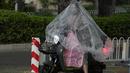 <p>Seorang wanita bermasker menggunakan plastik besar untuk menutupi tubuhnya saat hujan di Beijing (24/5/2022). Beijing memperpanjang perintah bagi pekerja dan pelajar untuk tinggal di rumah dan memerintahkan pengujian massal tambahan pada Senin ketika kasus COVID-19 meningkat di ibu kota China. (AP Photo/Ng Han Guan)</p>