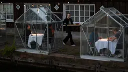 Staf menggunakan papan panjang untuk menyajikan makanan kepada pelanggan dalam kabin kaca "quarantine greenhouses" selama uji coba, ketika Belanda berjuang melawan penyebaran COVID-19, di restoran Mediamatic, Amsterdam pada 5 Mei 2020. (AP/Peter Dejong)