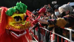 Orang-orang mencoba menyentuh singa saat pertunjukan barongsai di sebuah kuil pada hari kedua Tahun Baru Imlek Naga di Beijing pada 11 Februari 2024. (GREG BAKER/AFP)