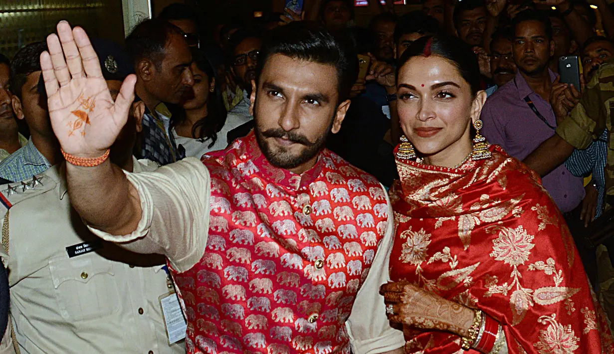 Pasangan pengantin baru, Ranveer Singh dan Deepika Padukone menyapa penggemar yang menyambut mereka di bandara internasional Mumbai, Minggu (18/11). Pasangan bintang Bollywood India itu baru saja kembali dari acara pernikahan mereka di Italia. (AFP)