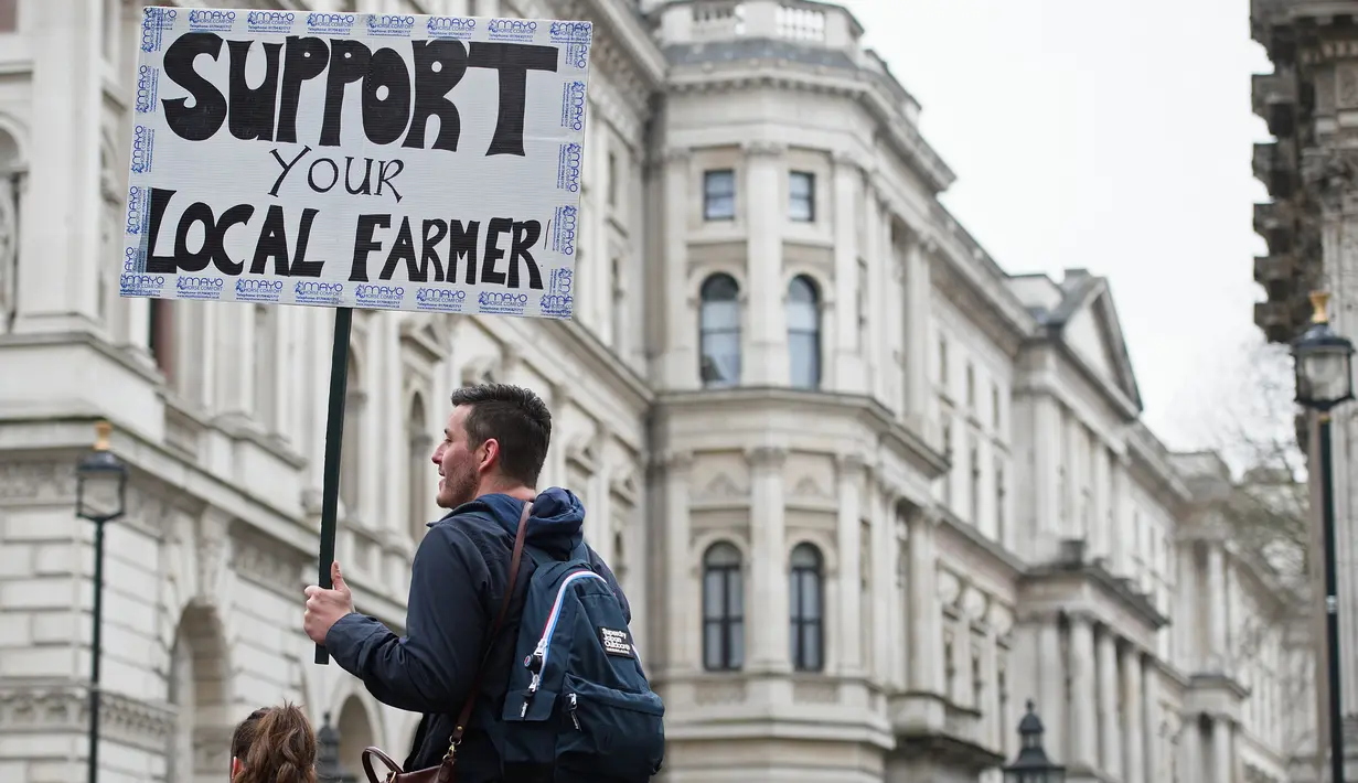 Seorang pria memegang plakat berisi tuntutannya dalam aksi protes oleh petani lokal di Downing Street, pusat kota London, Inggris, Rabu (23/3). (LEON Neal/AFP)