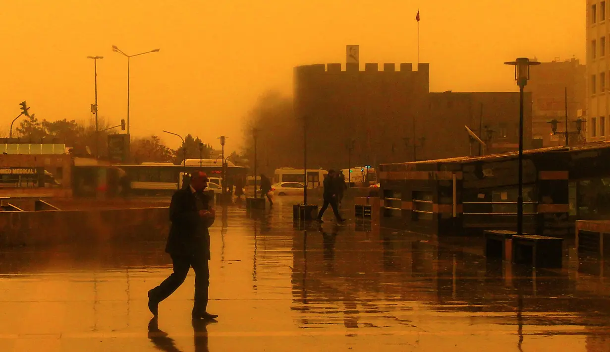 Sejumlah orang berjalan saat badai pasir menerjang Kota Diyarbakir di Turki, Jumat (19/1). Hempasan badai pasir tampak membuat pemandangan di Turki menjadi kuning kemerah-merahan. (AFP PHOTO / Ilyas AKENGIN)