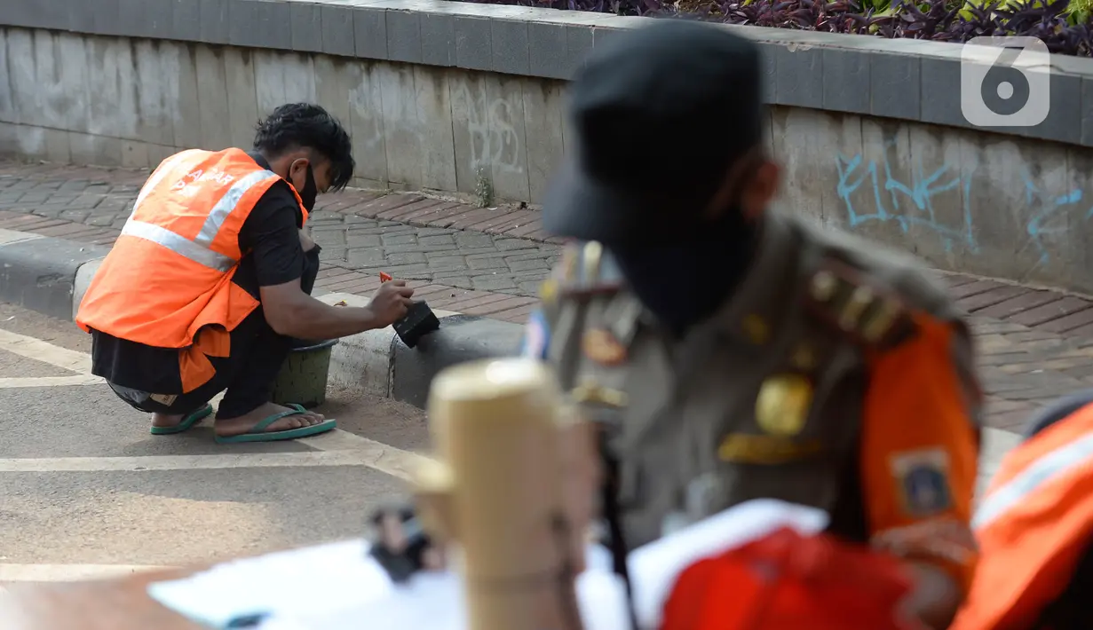 Warga terkena sanksi sosial mengcat pembatas jalan kepada warga pelanggar karena tidak menggunakan masker di Lebak Bulus, Jakarta, senin (14/09/2020). Pemerintah Provinsi DKI Jakarta memperketat kembali PSBB karena kasus Covid-19 terus mengalami peningkatan. (merdeka.com/Dwi Narwoko)