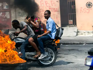 Pengendara sepeda motor melewati barikade ban yang terbakar saat terjadi protes krisis bahan bakar di Port-au-Prince, Haiti, Senin (16/9/2019). Krisis bahan bakar menyebabkan transportasi umum tidak beroperasi. (AP Photo/Dieu Nalio Chery)