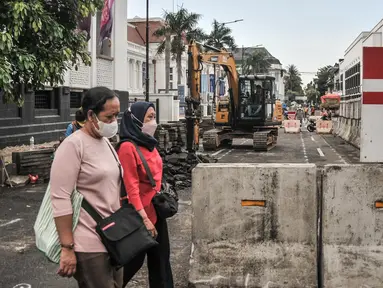 Pejalan kaki saat melintas di dekat proyek revitalisasi pedestrian kawasan Kota Tua, Jakarta, Minggu (27/3/2022). Jalur pedestrian itu akan diubah menjadi plaza pedestrian yang lebar sebagai bagian dari penataan kawasan Kota Tua yang rendah emisi (merdeka.com/Iqbal S Nugroho)