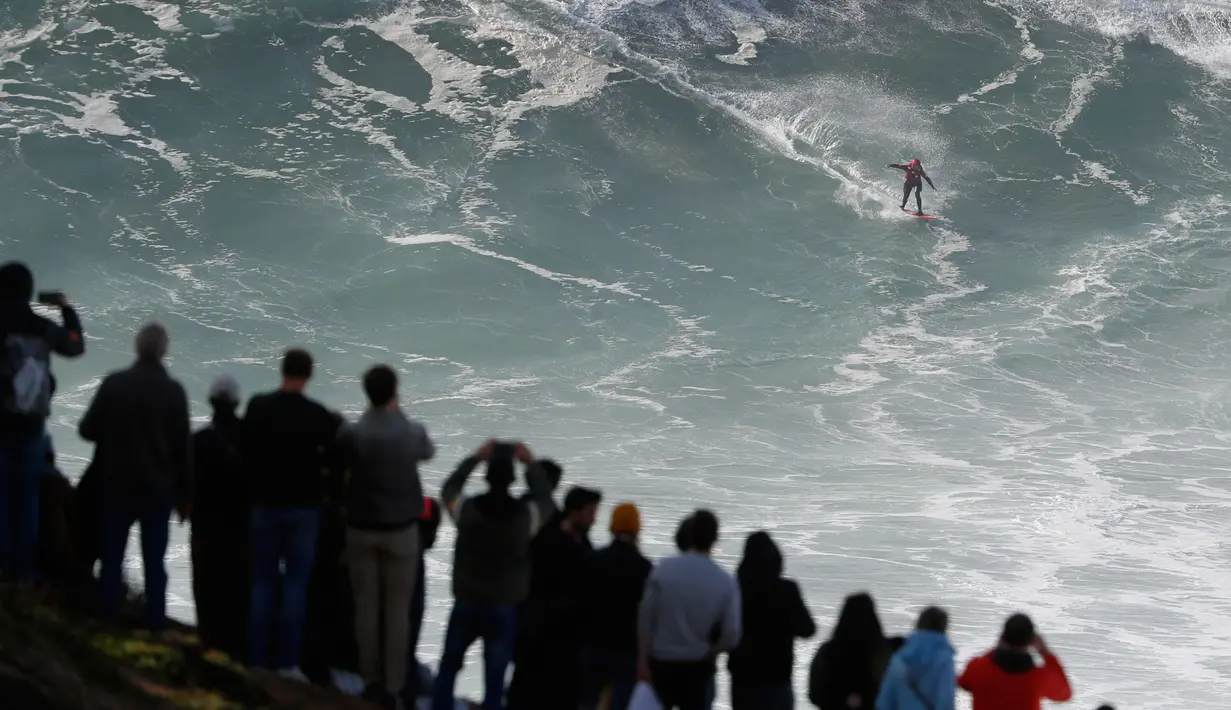 Penonton menyaksikan peselancar unjuk kebolehan dalam menaklukkan ombak besar di Praia do Norte atau Pantai Utara, Nazare, Portugal, Rabu (20/11/2019). Perairan Praia do Norte menjadi tempat uji nyali para peselancar dunia karena ombaknya yang bisa mencapai 30 meter. (AP Photo/Armando Franca)