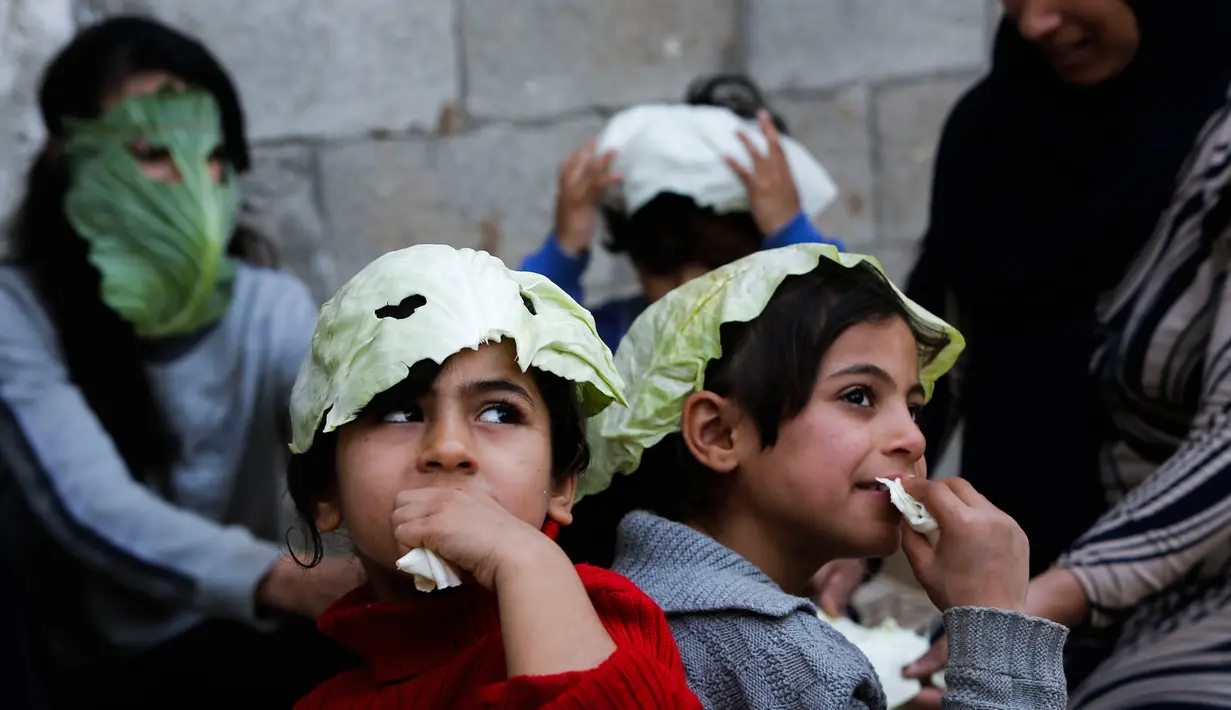 Anak-anak Palestina mengenakan masker yang terbuat dari kubis  saat bermain  di tengah pandemi Covid-19 di Beit Lahia di Jalur Gaza utara (16/4/2020). (AFP/Mohamed Abed)