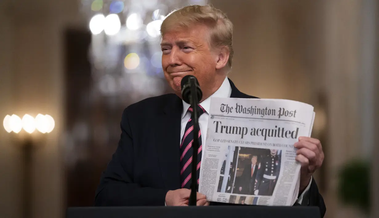 Presiden Donald Trump tersenyum saat menunjukkan surat kabar dengan tajuk utama bertuliskan "Trump dibebaskan" di Ruang Timur Gedung Putih, Washington (6/2/2020). Para senator AS memutuskan bahwa Trump tidak bersalah dalam sidang pemakzulan. (AP Photo/Evan Vucci)