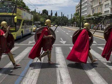 Sekelompok Pria berpakaian seperti tentara Yunani kuno menyeberang jalan sambil membawa tombak, perisai saat pertunjukan di Konstitusi (Syntagma) persegi di Athena, Yunani (21/6/2015). (REUTERS /Marko Djurica)