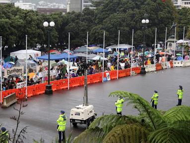 Para pengunjuk rasa (kiri) memadati halaman Parlemen ketika polisi (kanan) mengawasi pada hari kelima demonstrasi menentang pembatasan COVID-19 di Wellington, Selandia Baru, 12 Februari 2022. Aksi ini terinspirasi oleh demonstrasi serupa di Kanada. (MARTY MELVILLE/AFP)