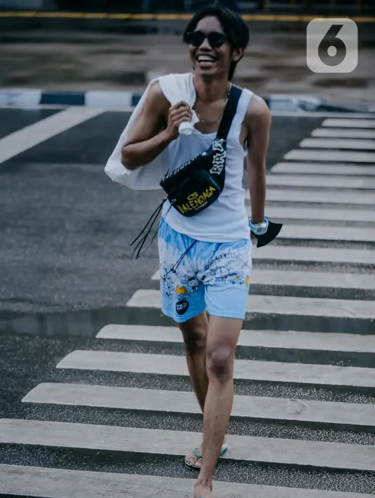 Seorang remaja mengenakan kaca mata berjalan melintasi zebra cross di Taman Sudirman, Jakarta, Rabu (6/7/2022). Tempat ini viral karena jadi ajang adu fashion anak Citayam, Bekasi hingga Bojong Gede. Mereka mengenakan kemeja flanel oversize, celana model 90-an seperti boot cut atau cutbray, sneakers klasik, dan tentu saja topi. (Liputan6.com/Faizal Fanani)