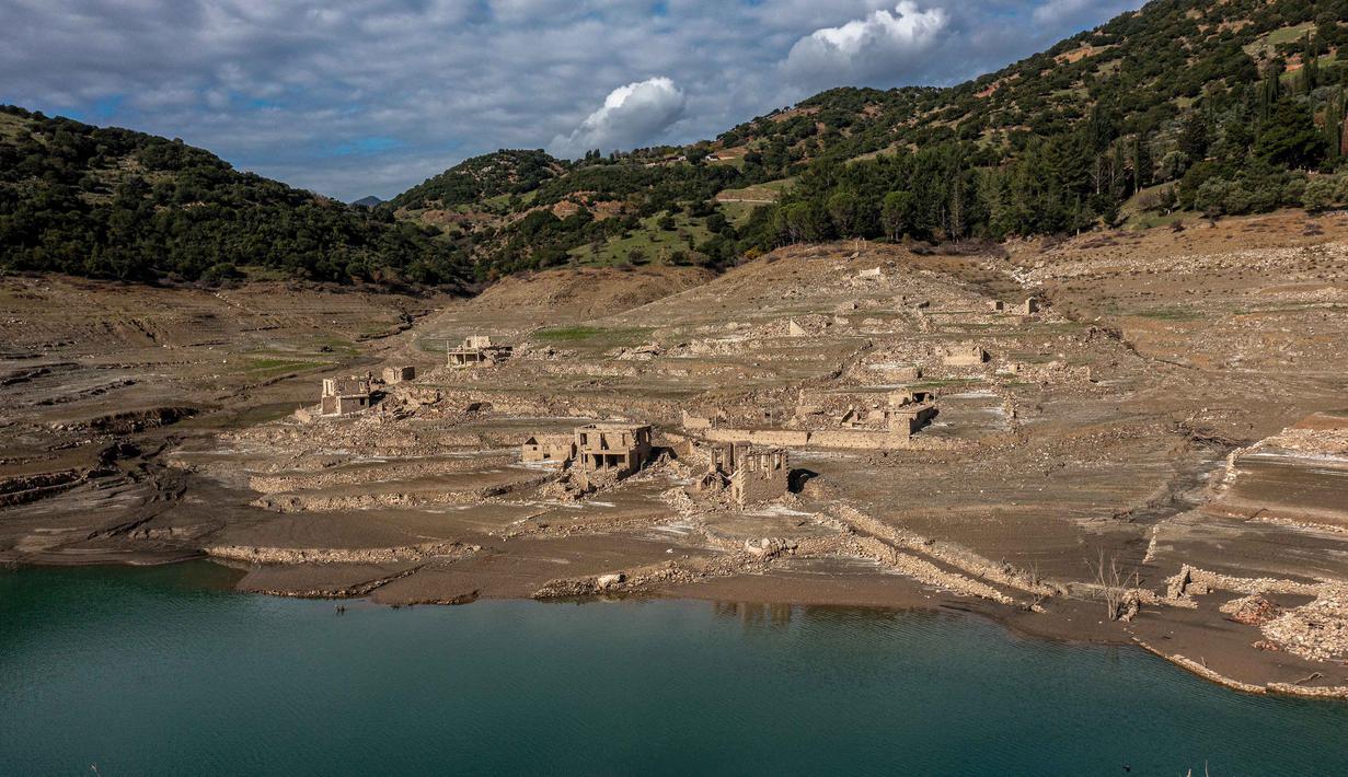Foto ini menunjukkan sisa-sisa rumah yang muncul kembali ketika permukaan danau buatan Mornos menurun akibat kekeringan, di desa Kallio, sekitar 240 km barat laut Athena, Yunani pada 3 November 2025. , ketika air surut, sisa-sisa desa, termasuk reruntuhan rumah, sekolah, dan bahkan lantai pertama dari beberapa bangunan, menjadi terlihat kembali. (Angelos TZORTZINIS/AFP)