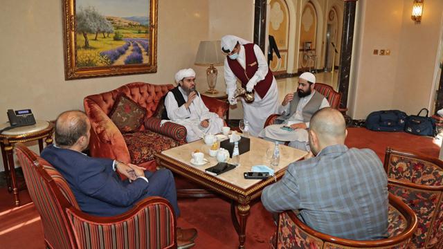 <span>Mantan utusan Taliban untuk Arab Saudi Shahabuddin Delawar (tengah) menyeruput kopi sebelum pertemuan dengan diplomat asing di Doha, Qatar, Selasa (12/10/2021). Taliban mengadakan pembicaraan dengan utusan Uni Eropa dan AS untuk mencari dukungan internasional. (KARIM JAAFAR/AFP)</span>