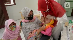 Bidan dibantu Kader Posyandu memberikan vaksin vitamin A dan imunisasi di Posyandu RW 20, Kelurahan Pondok Benda, Tangerang Selatan, Selasa (18/8/2020). Pemerintah sudah mengaktifkan pelayanan posyandu ketiga sejak pandemi Covid-19 dengan memperketat protokol kesehatan. (merdeka.com/Dwi Narwoko)