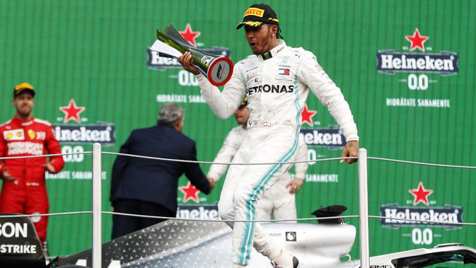 Pembalap Mercedes Lewis Hamilton berselebrasi membawa pialanya setelah berhasil menjuarai balapan GP Meksiko di Autodromo Hermanos Rodriguez, Mexico City (28/10/2019). Hamilton unggul 74 poin atas Bottas di posisi kedua klasemen dengan 289 poin. (AP Photo/Eduardo Verdugo)