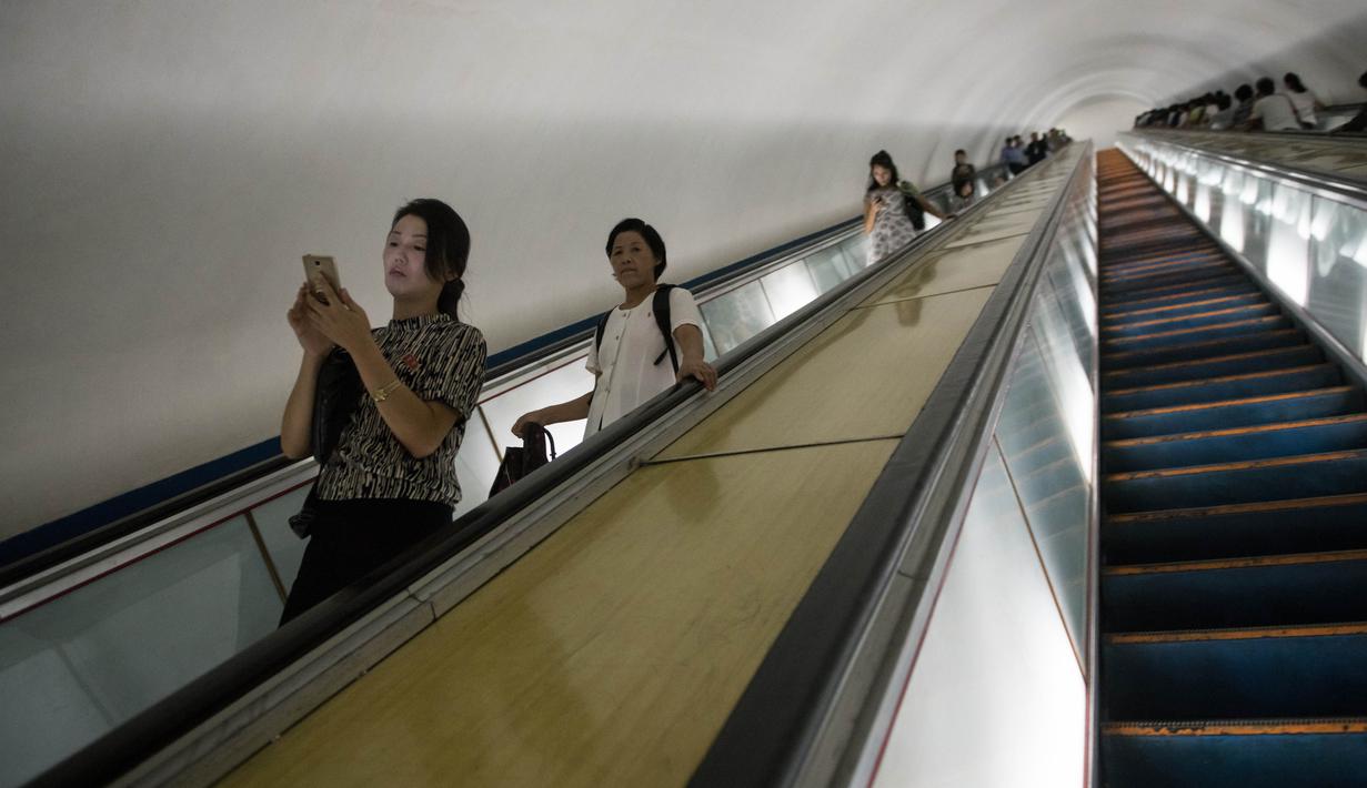 Komuter melihat ponselnya sambil menggunakan eskalator di stasiun kereta bawah tanah Pyongyang, Korea Utara, 6 September 2018. Ternyata kebiasaan melihat gawai di kereta pun tidak jauh berbeda, meskipun tidak banyak. (AFP / Ed JONES)