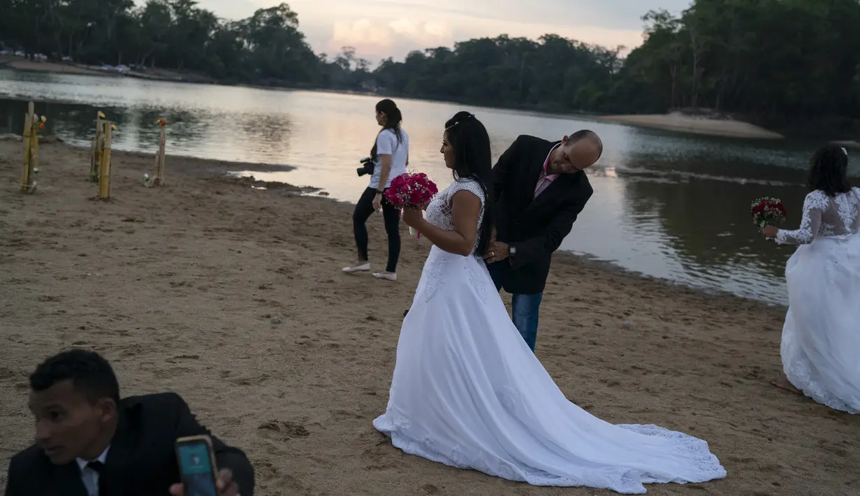 Suami dari Eliene Pereira Francisco membantu istrinya merapikan gaun setelah difoto untuk album pernikahan dengan latar belakang hutan hujan Amazon di pantai sungai Jamanxim, Brasil (2/9/2019). Mereka memutuskan untuk merayakan hari ini dengan pemotretan di tepi sungai. (Foto AP / Leo Correa)
