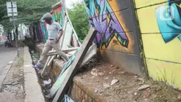 Seorang  pria melintas dekat tembok Jalan Juanda yang ambruk di kawasan Depok, Jawa Barat, Senin (2/12/2019). Kondisi tembok yang dipenuhi mural tersebut mulai rapuh dan sebagian sisinya telah ambruk serta miring sehingga membahayakan pejalan kaki. (Liputan6.com/Immanuel Antonius)