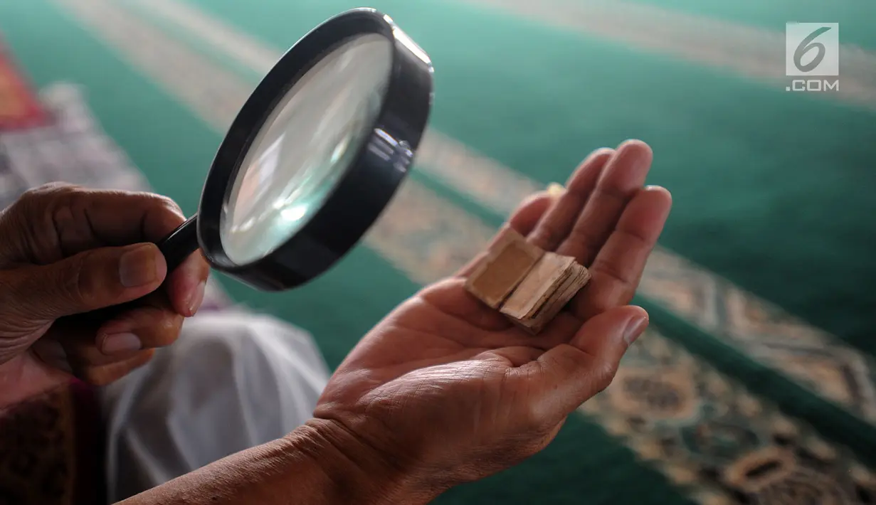 Kyai Tubagus Muhammad Tamyiz membaca Alquran mini bertinta emas dengan kaca pembesar di Masjid Jami Darusalam, Bogor, Kamis (24/5). Alquran mini itu benda bersejarah peninggalan pahlawan zaman kolonial, Pangeran Wijaya Kusuma. (Merdeka.com/Arie Basuki)