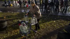 Perempuan lansia mendorong alat bantu jalan yang penuh dengan botol plastik setelah diisi ulang ke dalam tangki, di pusat kota Mykolaiv, Ukraina, Senin (24/10/2022). Sejak pertengahan April warga Mykolaiv telah hidup tanpa pasokan air minum. (AP Photo/Emilio Morenatti)
