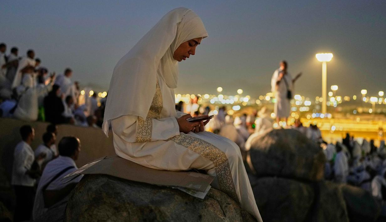 Seorang jemaah Muslim menggunakan telepon seluler untuk membaca ayat-ayat dari Al-Quran di atas bukit berbatu yang dikenal sebagai Jabal Rahmah atau Gunung Rahmat, di Dataran Arafah, selama ibadah haji tahunan di dekat kota suci Mekah, Arab Saudi, Selasa 26 Mei 2026. (AP Photo/Altaf Qadri)