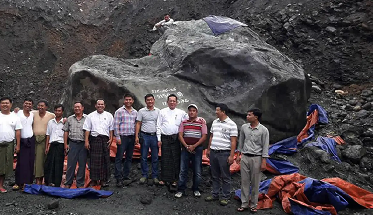 Pejabat setempat dan penambang berpose di depan batu giok yang ditemukan di lokasi tambang di negara bagian Kachin, Myanmar, Kamis (20/10). Sang pemilik mengaku tidak memiliki alat untuk memindahkan bongkahan yang diduga bernilai Rp2,2 T itu. (STR/AFP)