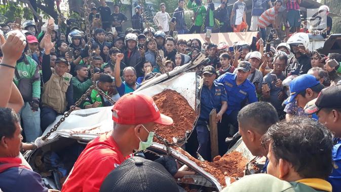 Warga berkerumun menyaksikan proses evakuasi bangkai mobil kecelakaan maut yang hancur tertindih badan truk muatan tanah di Karawaci, Tangerang, Kamis (1/8/2019). Sopir truk yang menimpa mobil dan menewaskan 4 orang itu kabur setelah kecelakaan maut terjadi. (/Pramita Tristiawati)